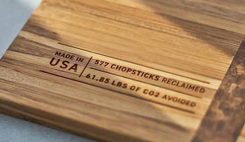 The corner of a cutting board made of recycled chopsticks, reading Renew, Made in the USA, 577 chopsticks reclaimed, 61.85 pounds of CO2 avoided.