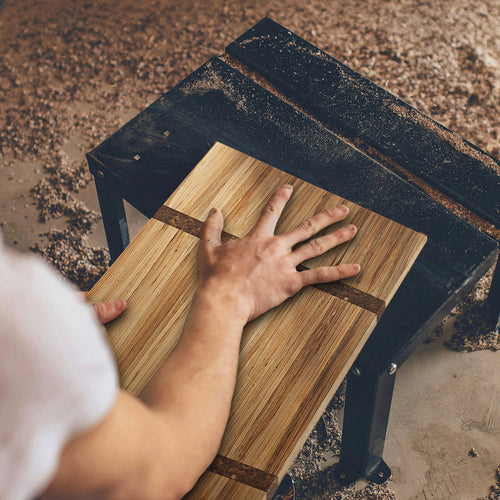 A cutting board made from recycled chopsticks being sanded in a workshop by hand.