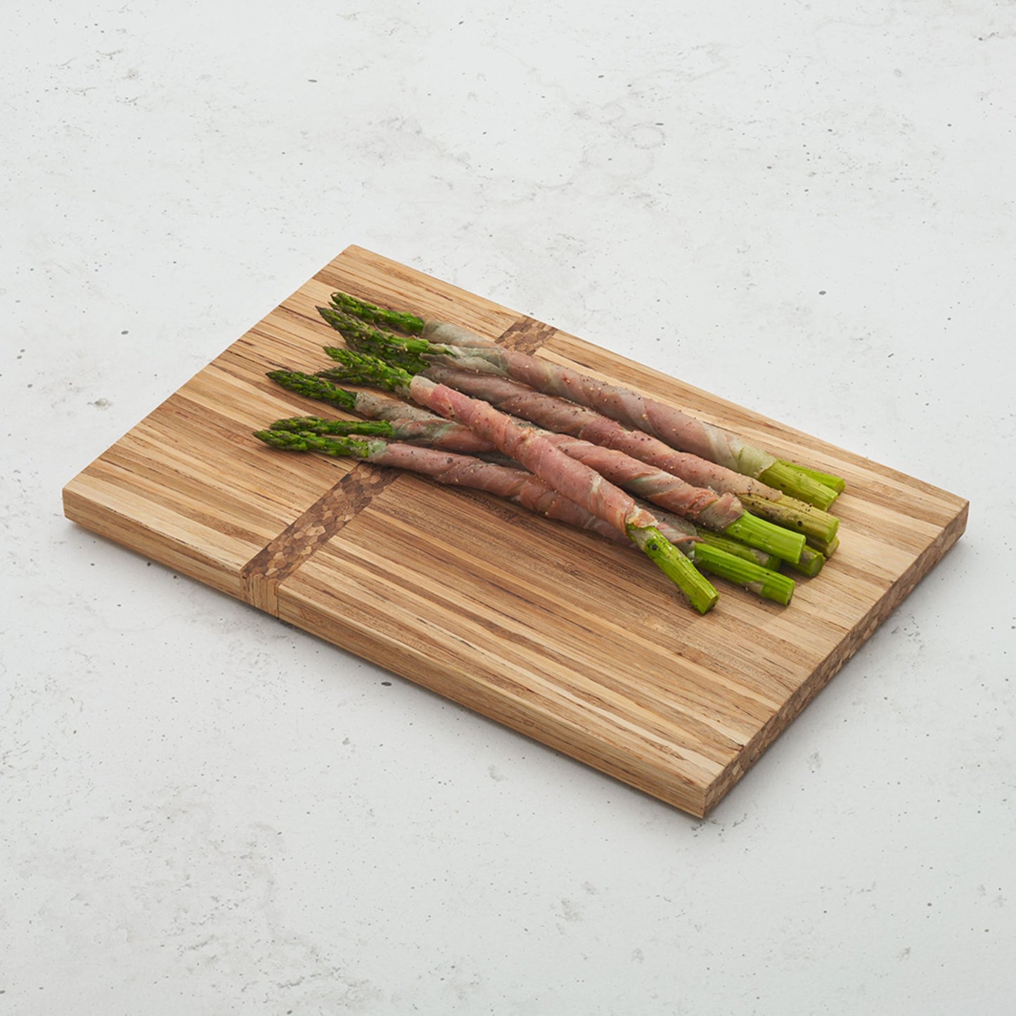 gather and graze serving board on a countertop with a bundle of asparagus wrapped in prosciutto on top