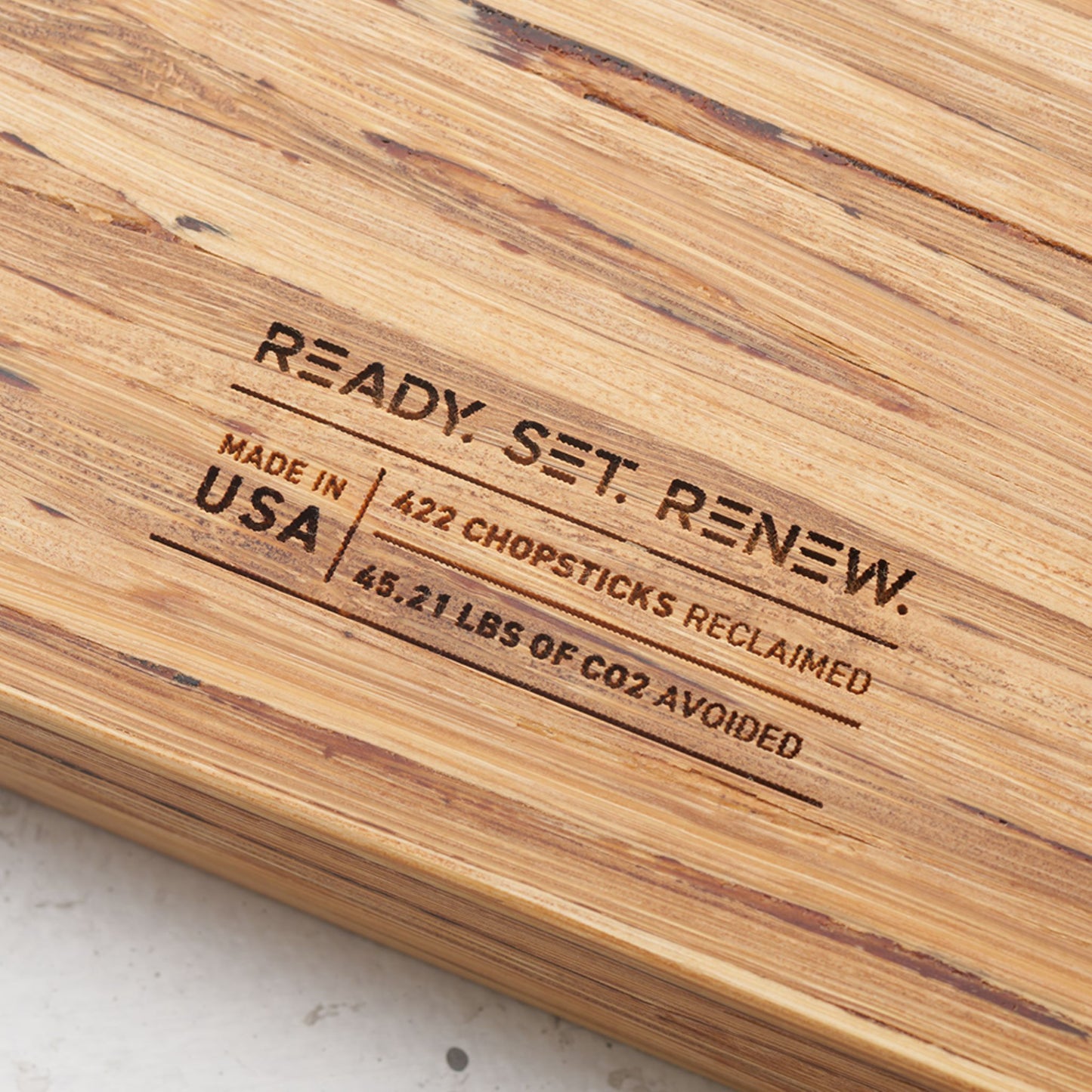 Close up view of the stamp on the back of the board that reads renew made in the usa four hundred and twenty two chopsticks reclaimed and forty five point twenty one pounds of co2 avoided