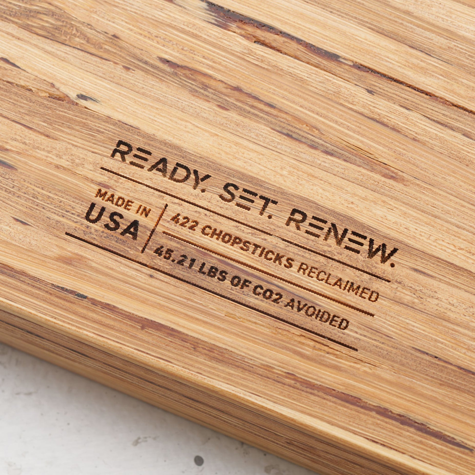 Close up view of the stamp on the back of the board that reads renew made in the usa four hundred and twenty two chopsticks reclaimed and forty five point twenty one pounds of co2 avoided