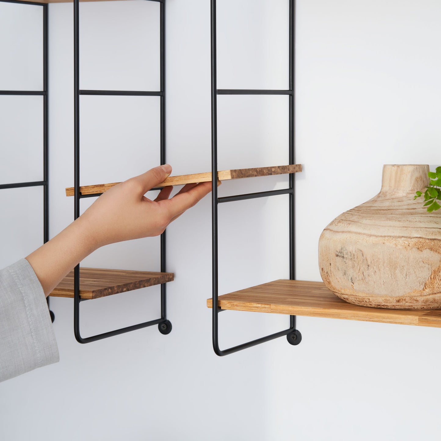 Close up view of a woman placing adjusting one of the wood chopstick shelf planks on the modular wall shelf