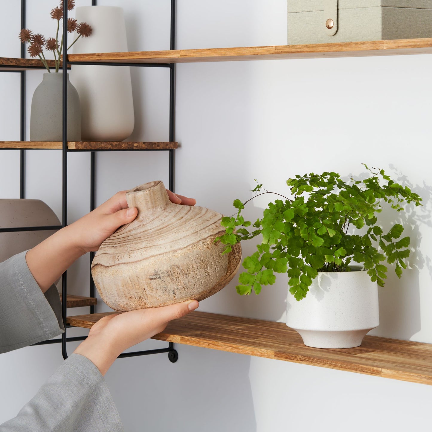 Close up view of a woman placing pottery on the wood chopstick shelf of the modular wall shelf