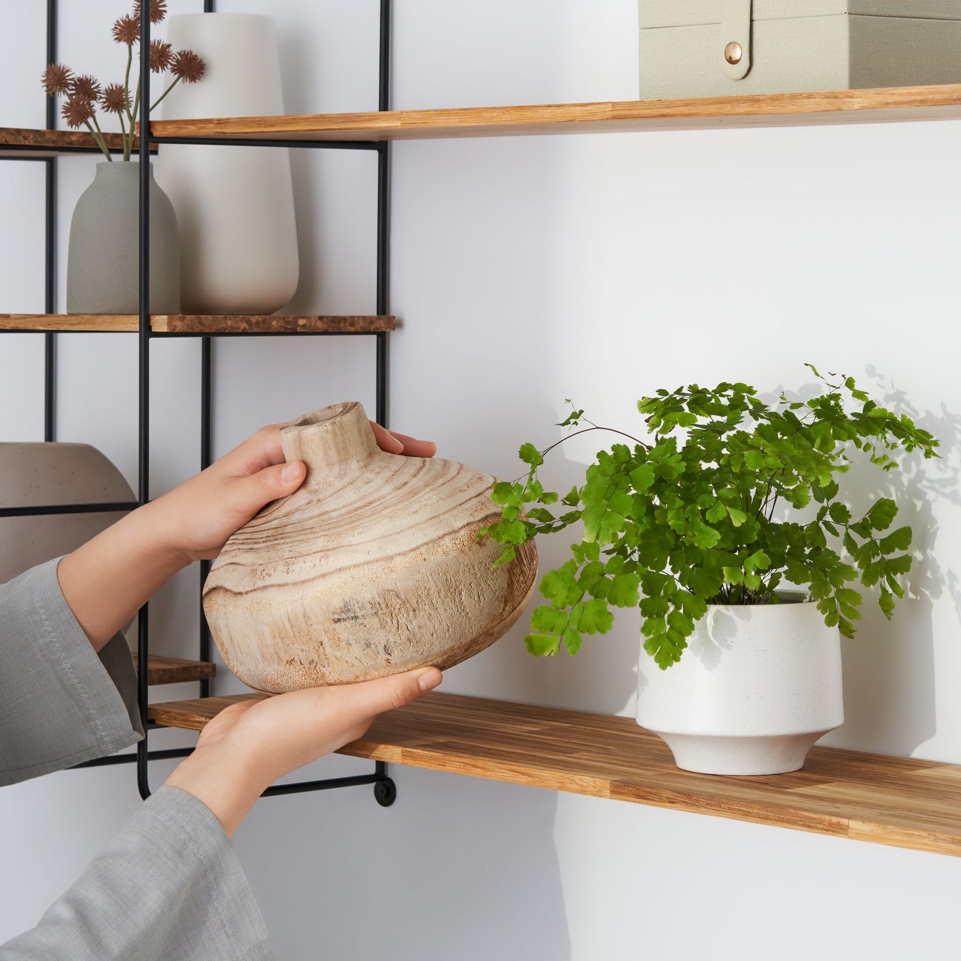 Close up view of a woman placing pottery on the wood chopstick shelf of the modular wall shelf