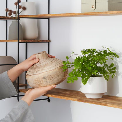 Close up view of a woman placing pottery on the wood chopstick shelf of the modular wall shelf